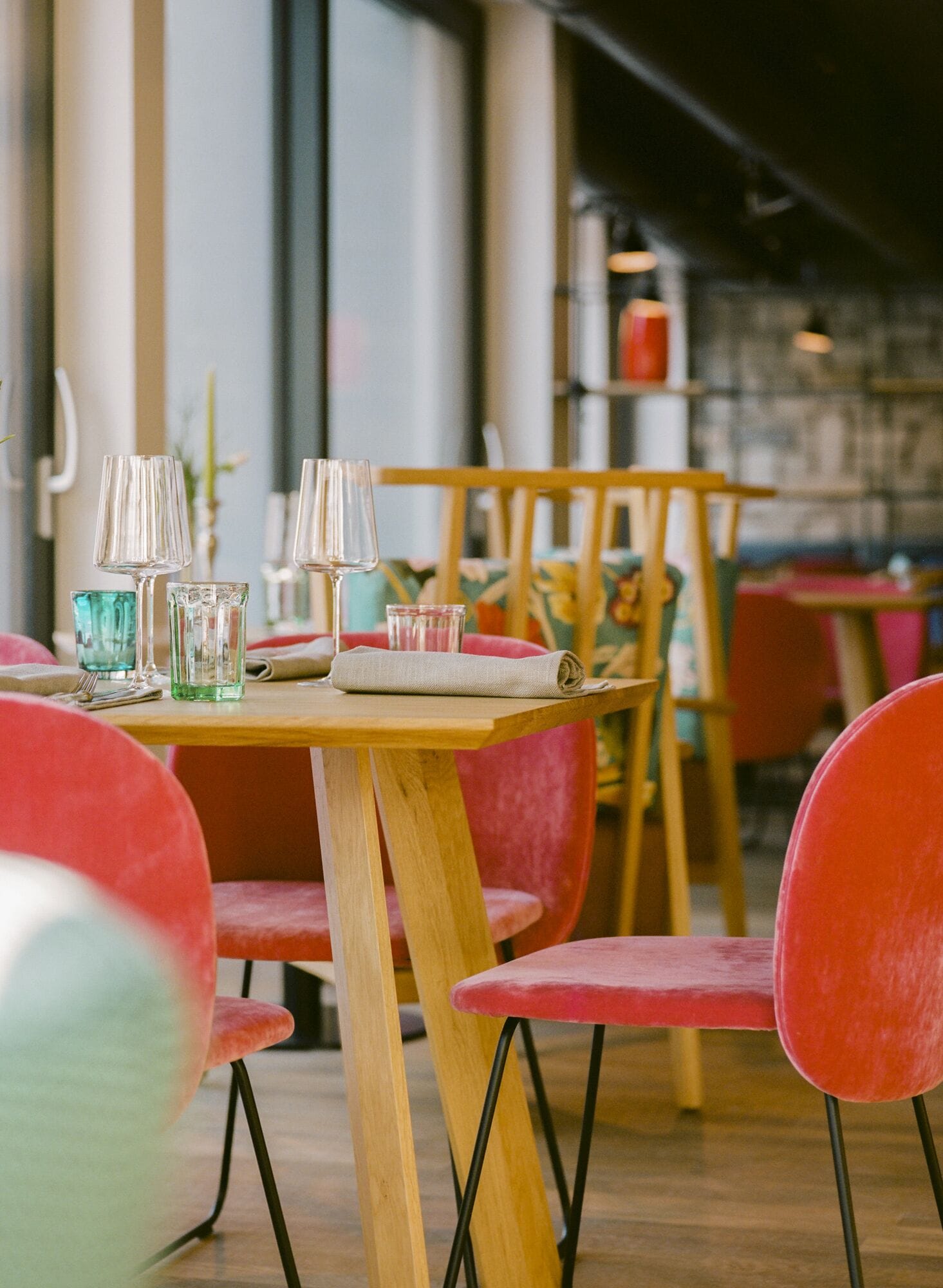 Interior de restaurante con mesas de madera y sillas rojas, destacando copas de vidrio transparente y servilletas tejidas.