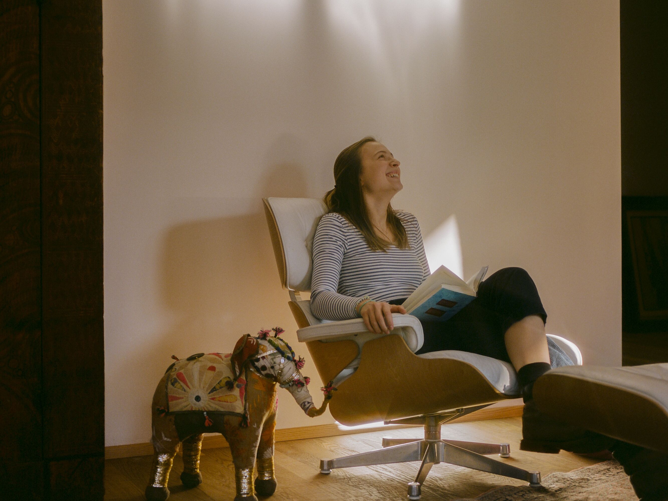 Una persona sentada en una silla leyendo un libro en una habitación con una escultura decorativa de elefante en el suelo.
