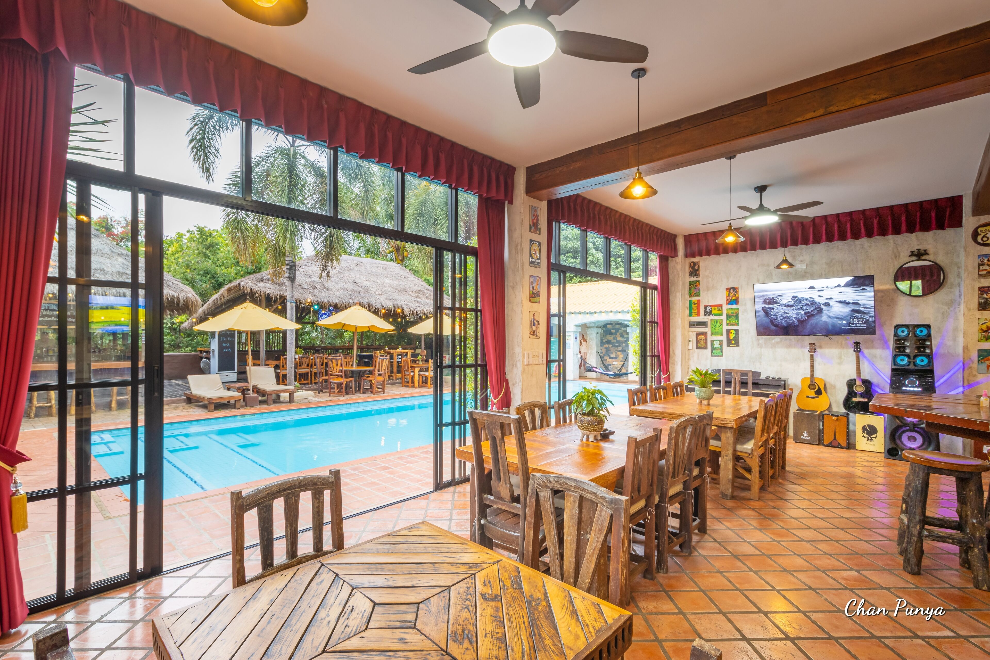 A restaurant with a pool view, wooden furniture, and a TV screen.