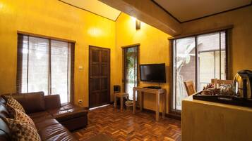 Una sala de estar con un sofá de cuero marrón, un televisor sobre un mueble de madera y una cafetera en una mesa.