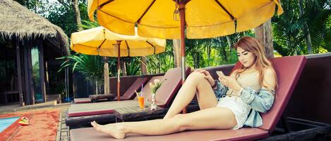 A poolside lounge area with sun loungers, yellow umbrellas, and a thatched-roof structure.