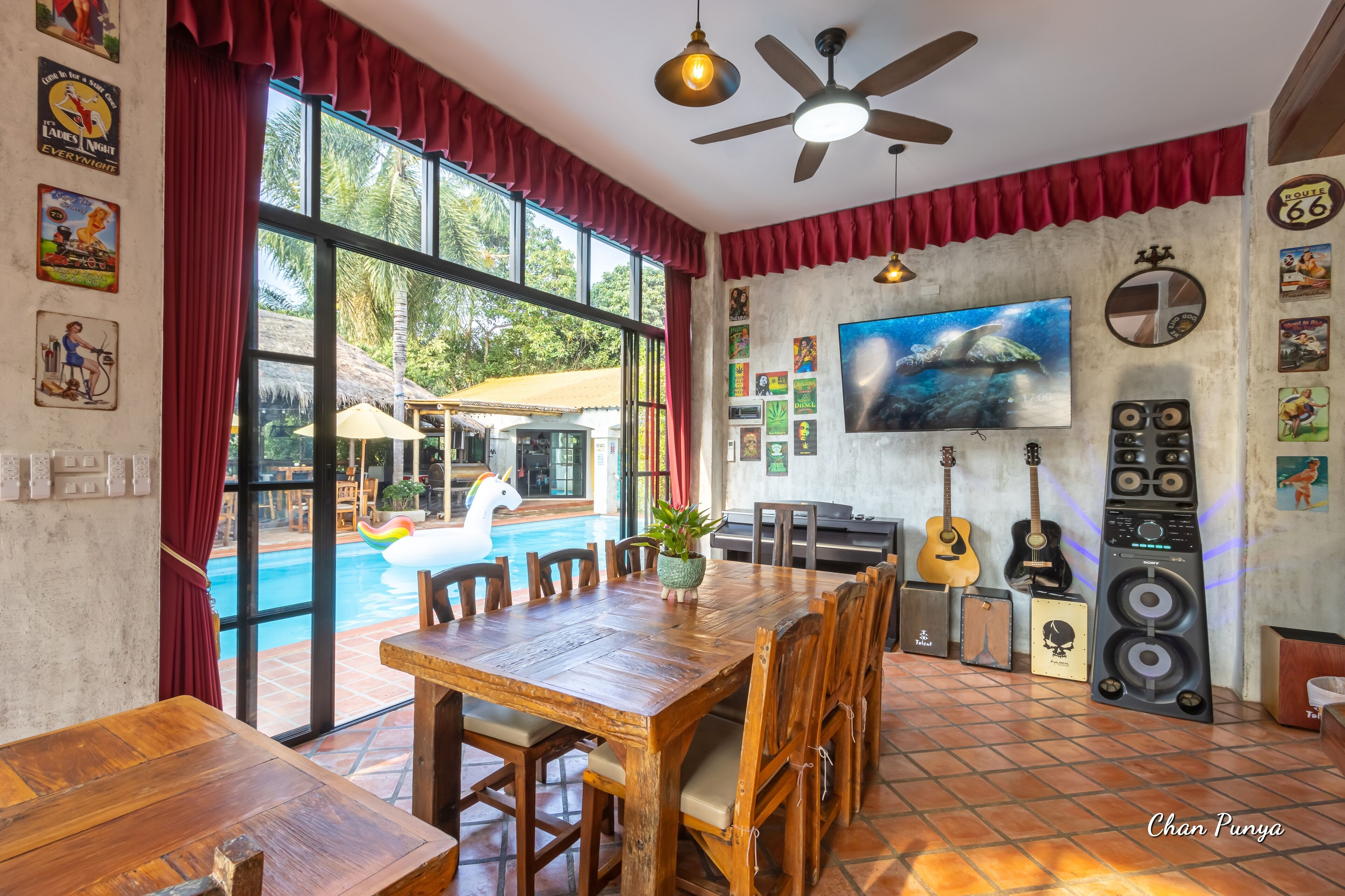 A spacious room with a large wooden dining table, a ceiling fan, and a TV on the wall.