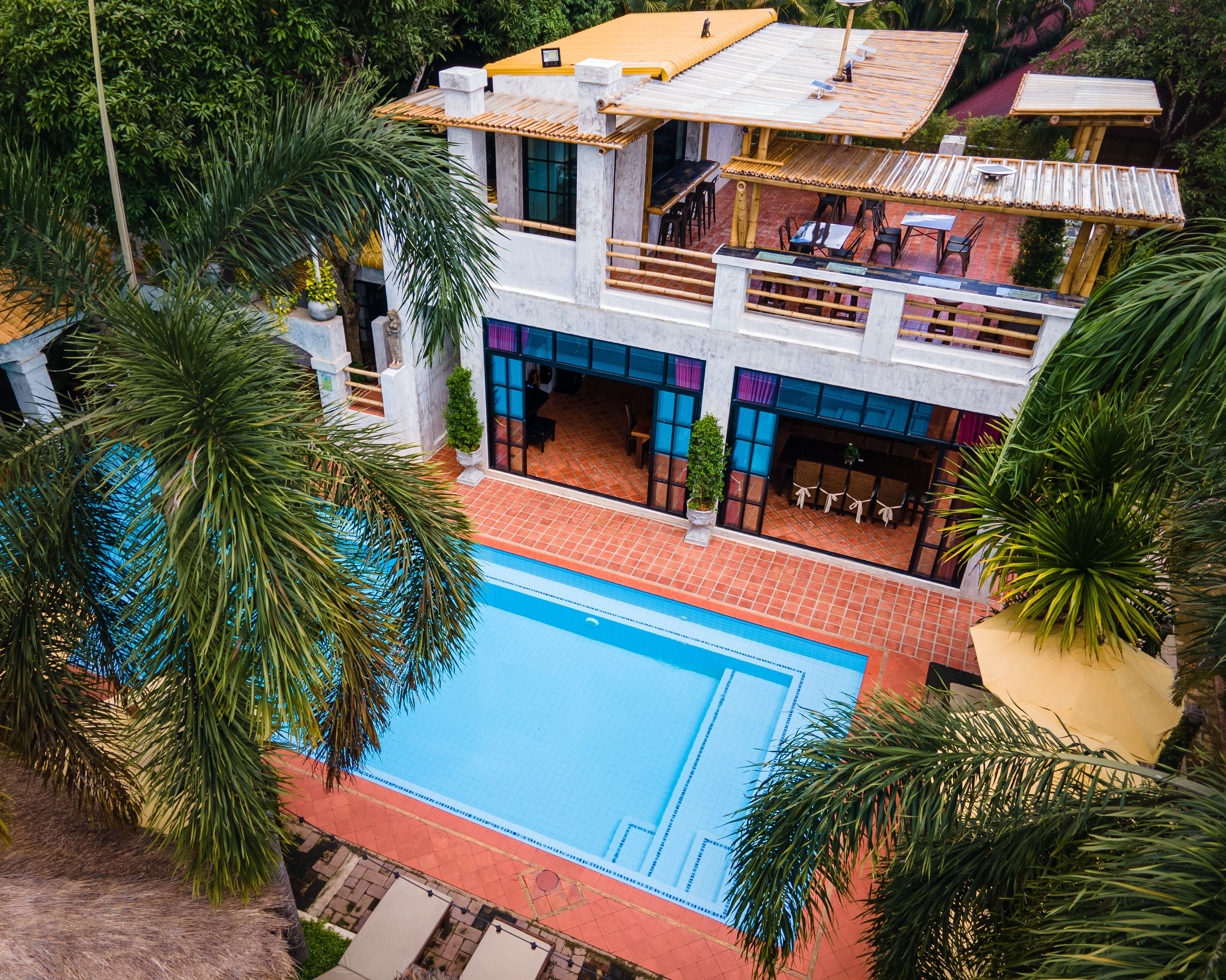 Un edificio de dos pisos con piscina, zona de estar al aire libre y abundante vegetación.