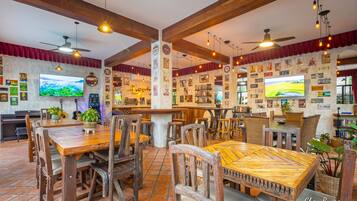 Un restaurant avec des tables et des chaises en bois, un téléviseur et diverses décorations murales.