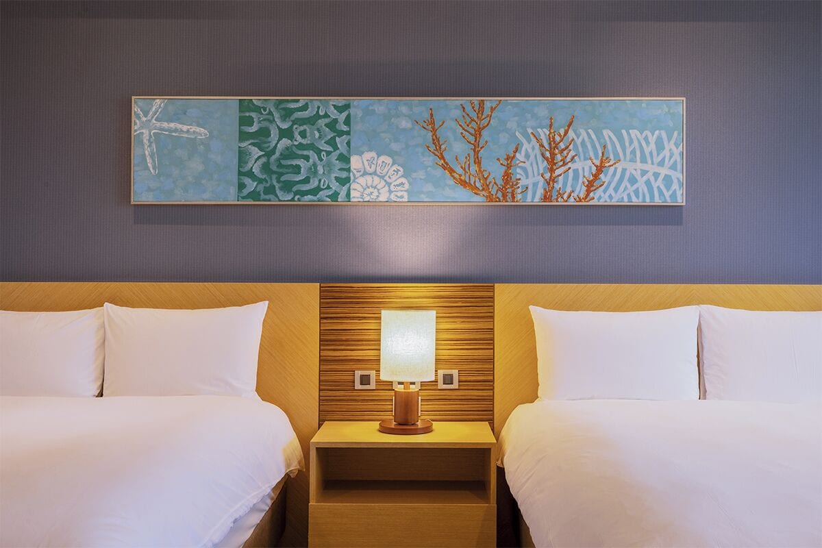 Une chambre d’hôtel avec deux lits, une table de chevet avec une lampe et un grand tableau abstrait accroché au mur.