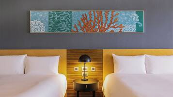 A hotel room with two beds, a wooden headboard, a wall-mounted artwork depicting coral and sea life, and a bedside table with a lamp.