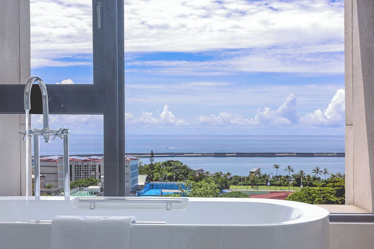 A bathroom with a bathtub and a view of the ocean and buildings.