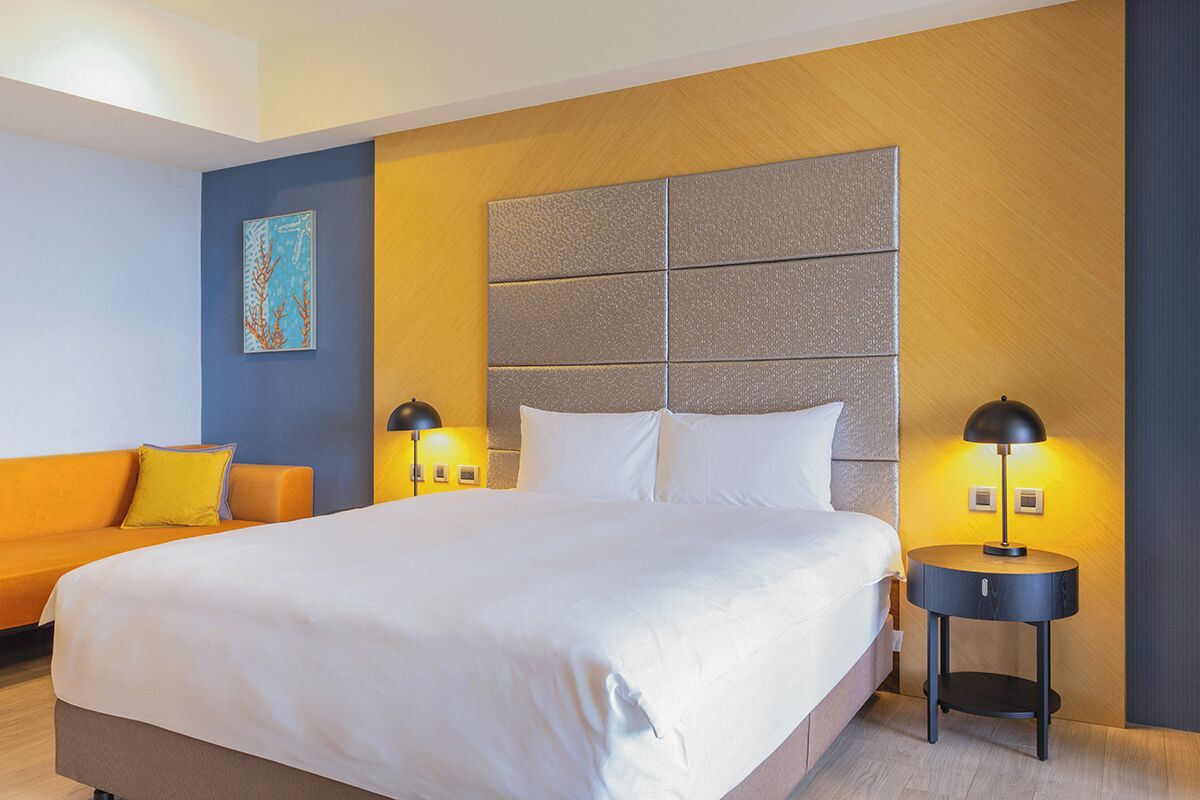 A hotel room with a large bed, a sofa, and two bedside tables with lamps.