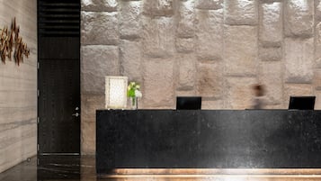 Un mostrador de recepción con un fondo de pared de piedra, una puerta de madera oscura y un jarrón con flores verdes.