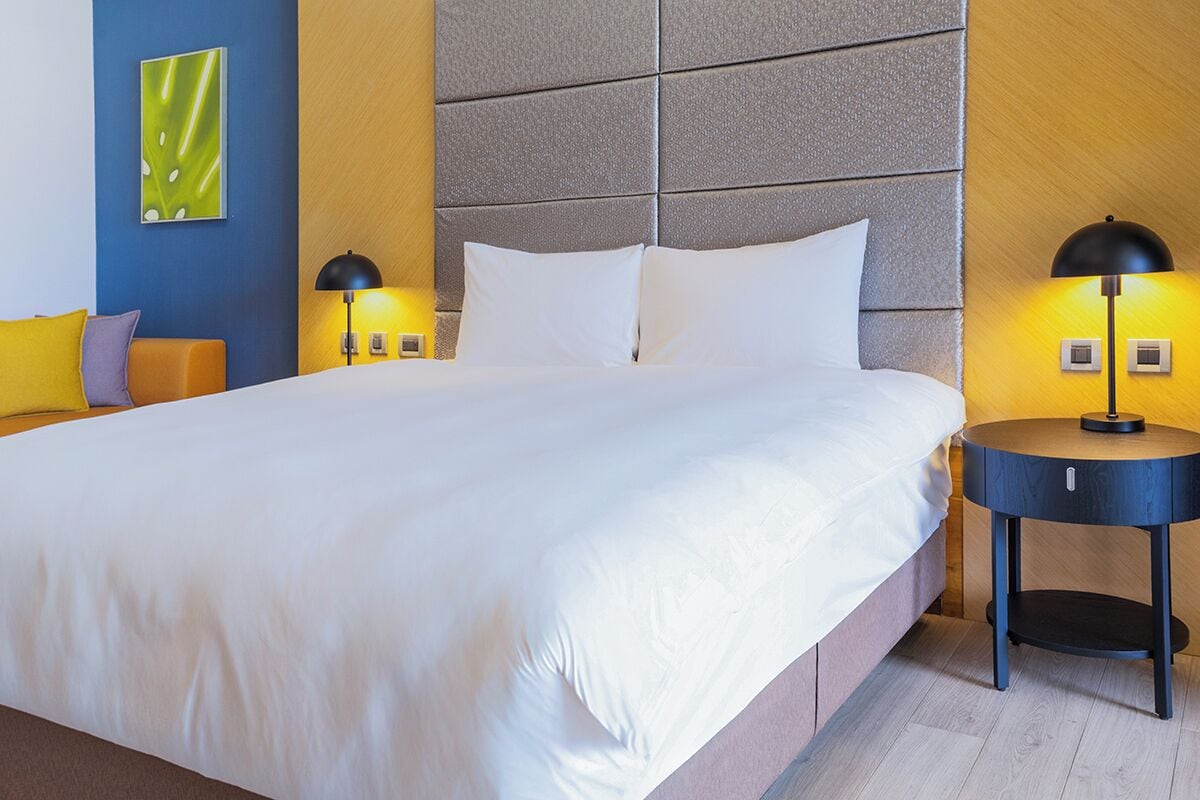 Una habitación de hotel con una cama grande, dos mesitas de noche con lámparas, un cabecero y una obra de arte colgada en la pared.