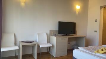 A hotel room with a bed, a desk with a computer, two white chairs, and two wall-mounted lights.