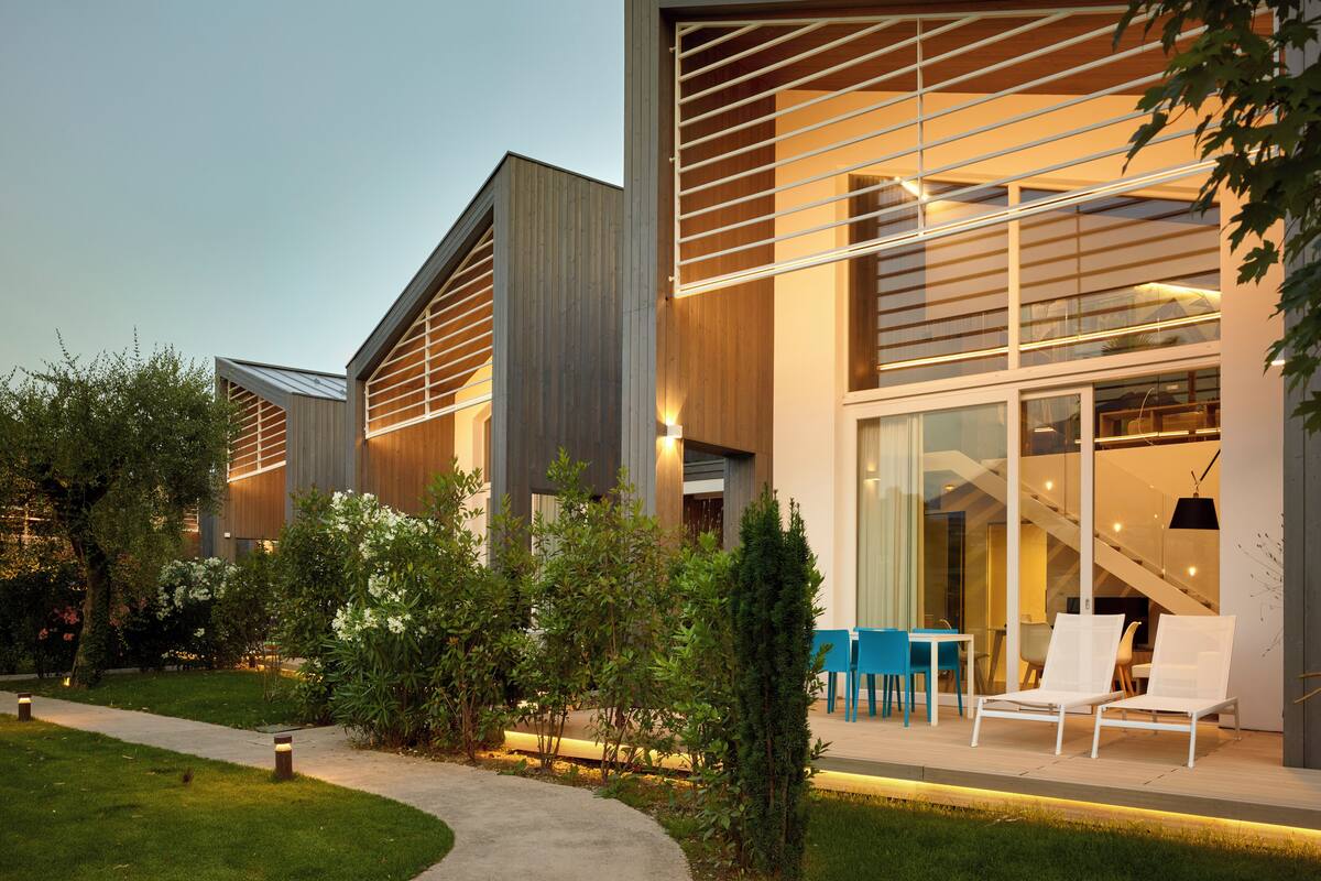 A modern building with large windows, a covered outdoor seating area, and a pathway leading to the entrance.