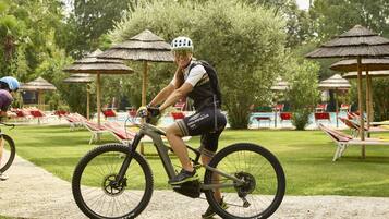 A person riding a bicycle on a path with a pool and lounge chairs in the background.
