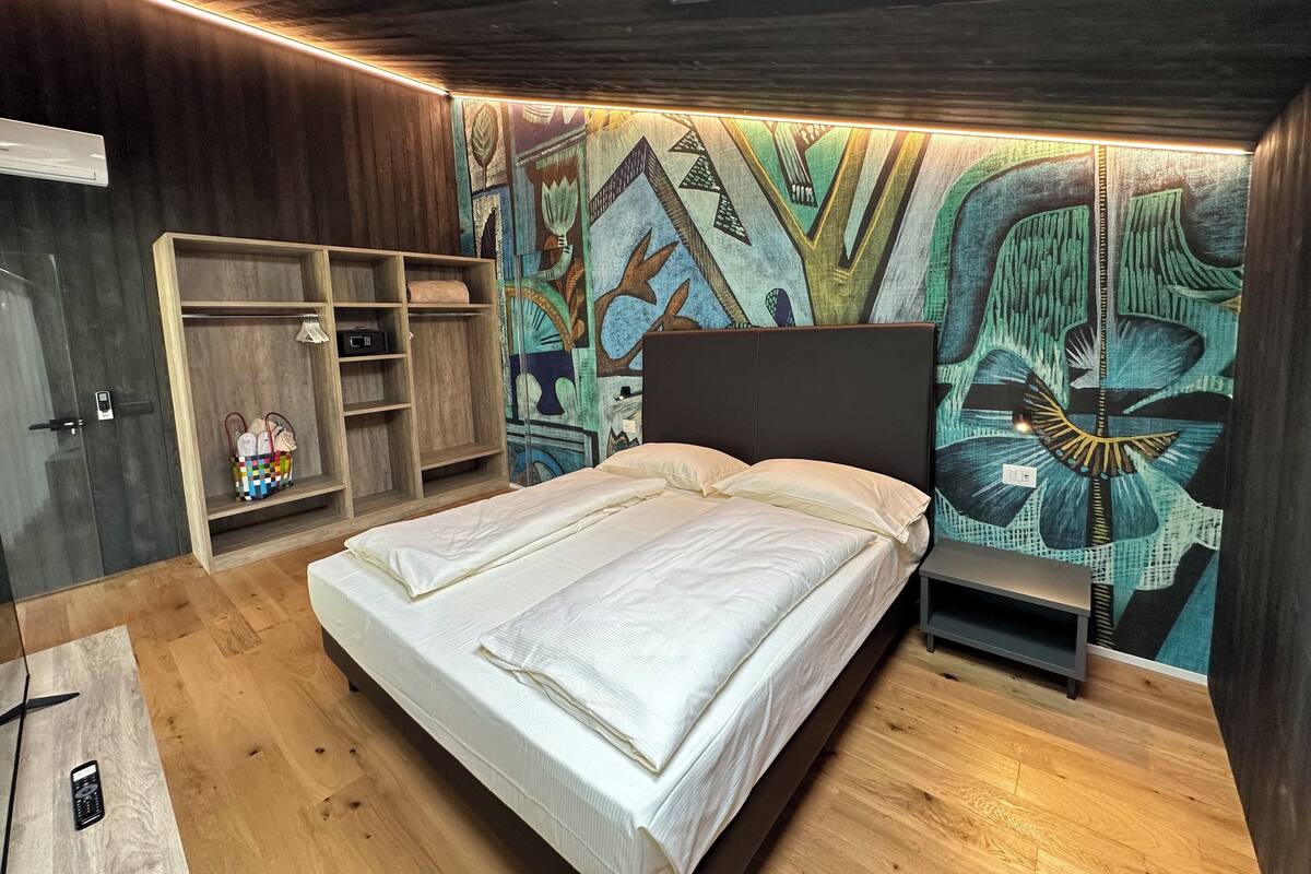 A bedroom with a bed, wooden wardrobe, and a colorful mural on the wall.