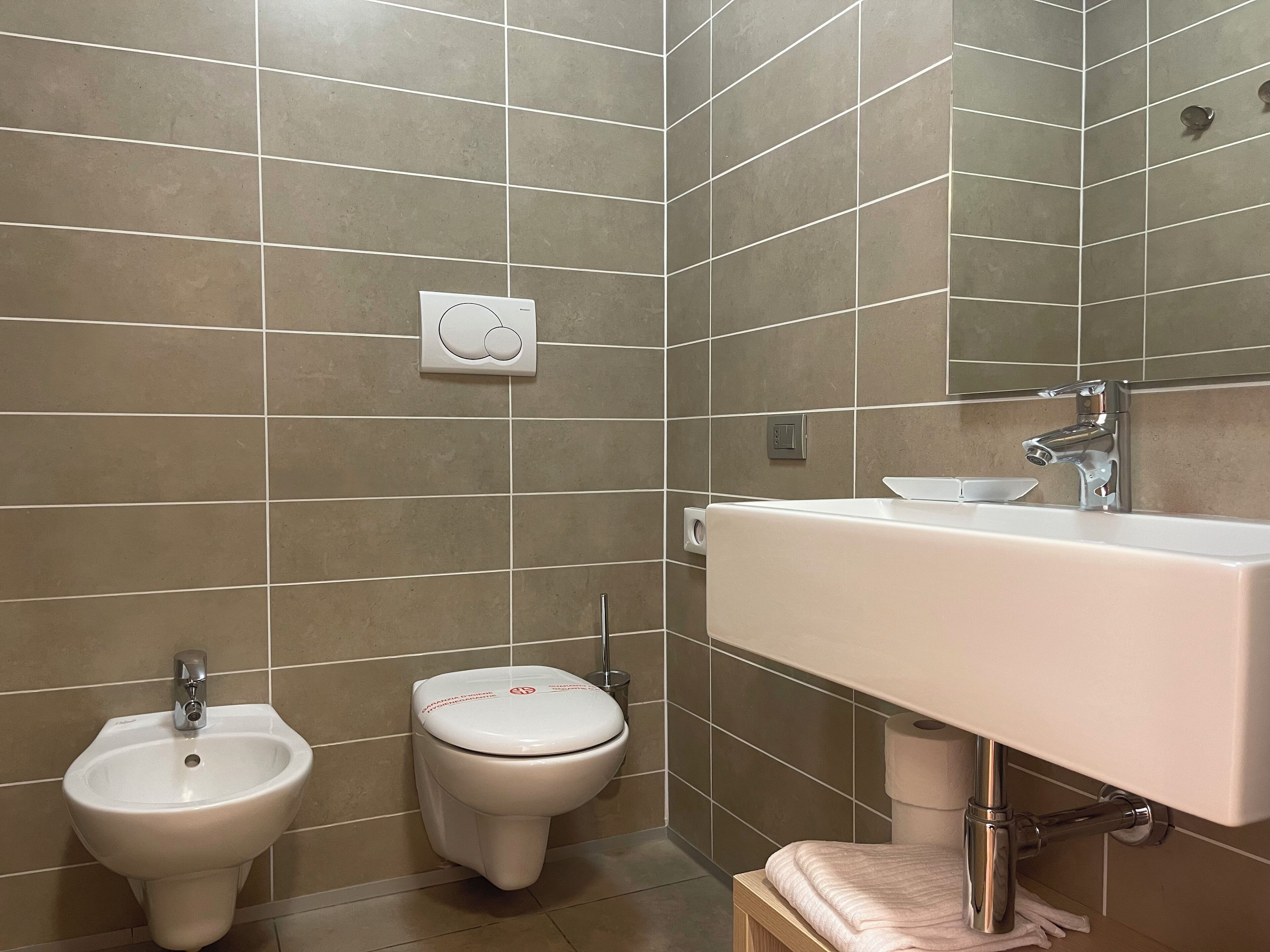 A modern bathroom with a bidet, toilet, sink, and a mirror.
