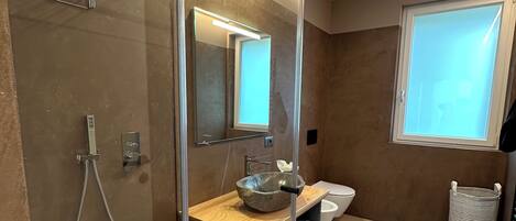 A modern bathroom with a glass-enclosed shower, a wooden vanity, a large mirror, and a toilet.