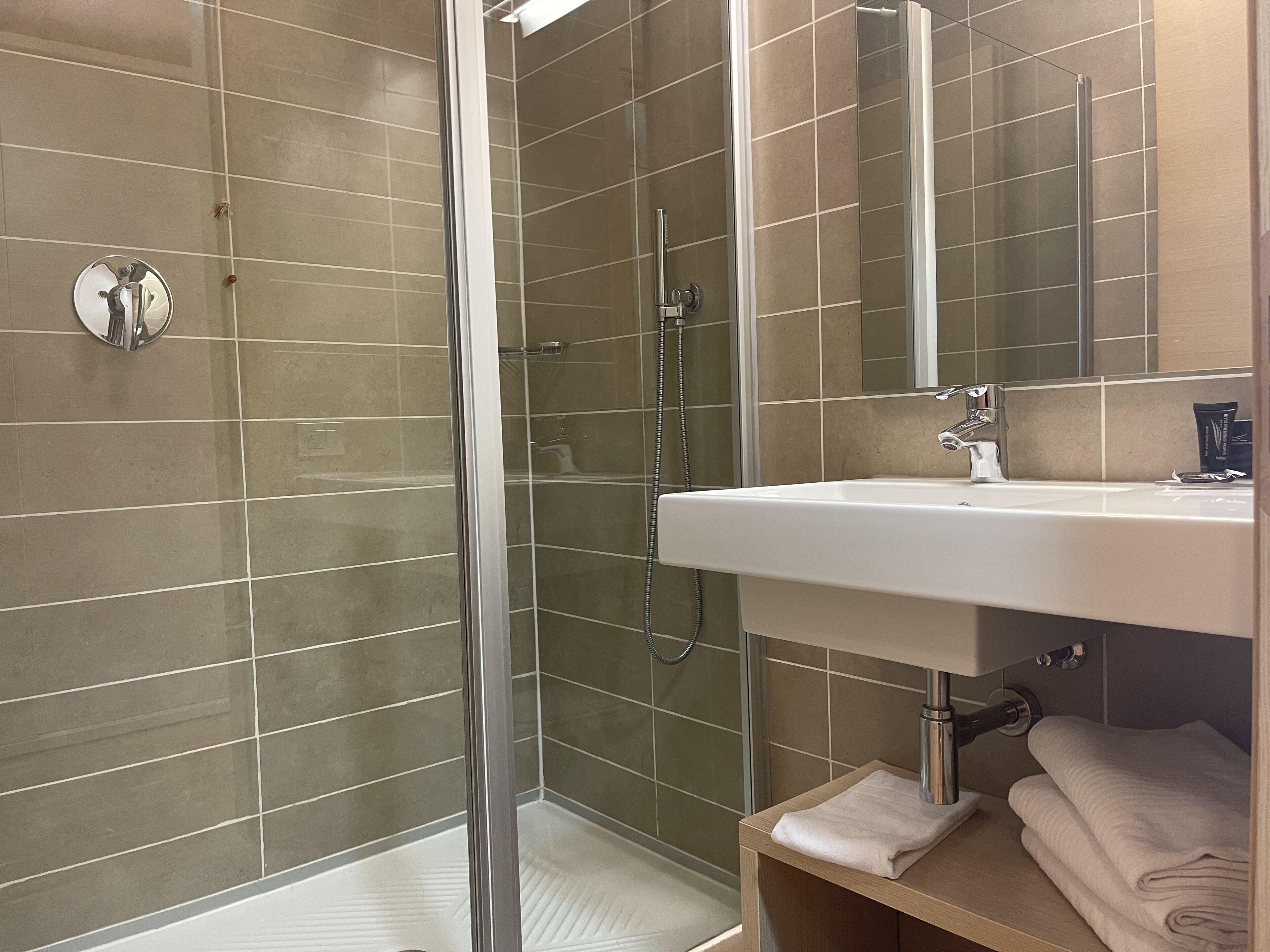 Ein modernes Badezimmer mit einer begehbaren Glasdusche, einem weißen Waschbecken und einem Spiegel darüber.