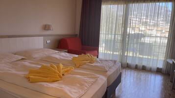 A hotel room with two beds, a red chair, a lamp, and a view through sheer curtains.