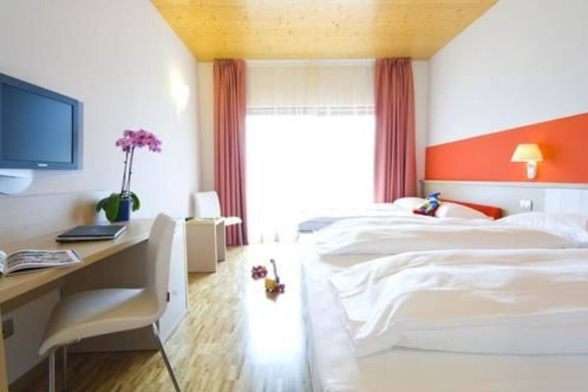 A hotel room with a bed, a desk with a chair, a television, and a window with curtains.