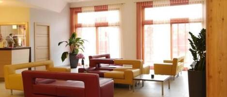 A modern hotel lobby with yellow and red sofas, a coffee table, and large windows with curtains.