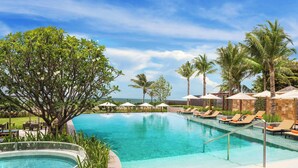 Une piscine entourée de chaises longues et de parasols, bordée de palmiers et offrant une vue sur l’océan.