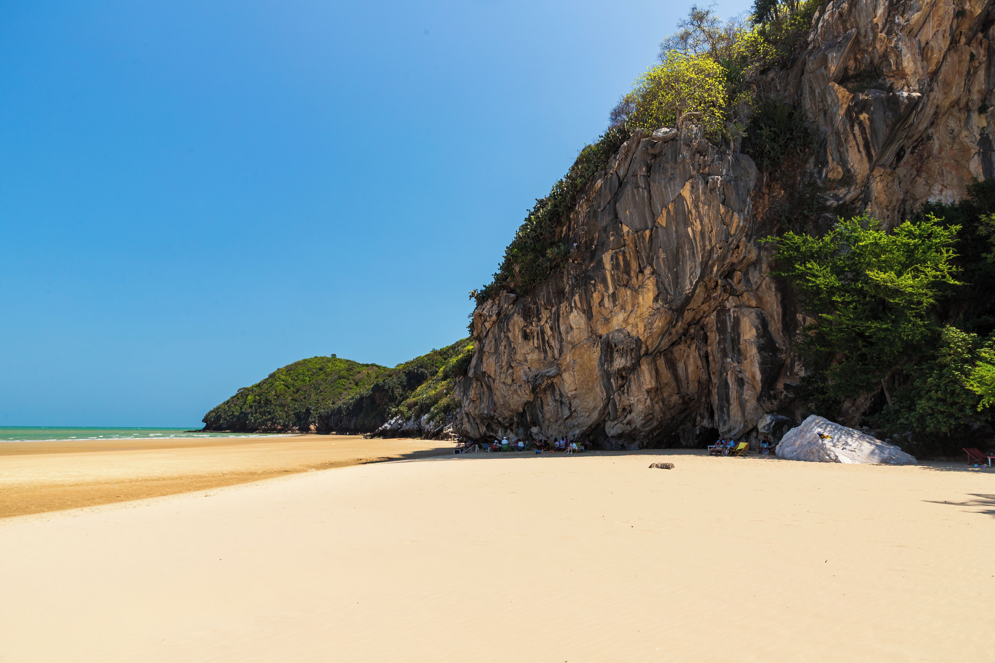 A beach with a rocky cliff and a clear sky.
