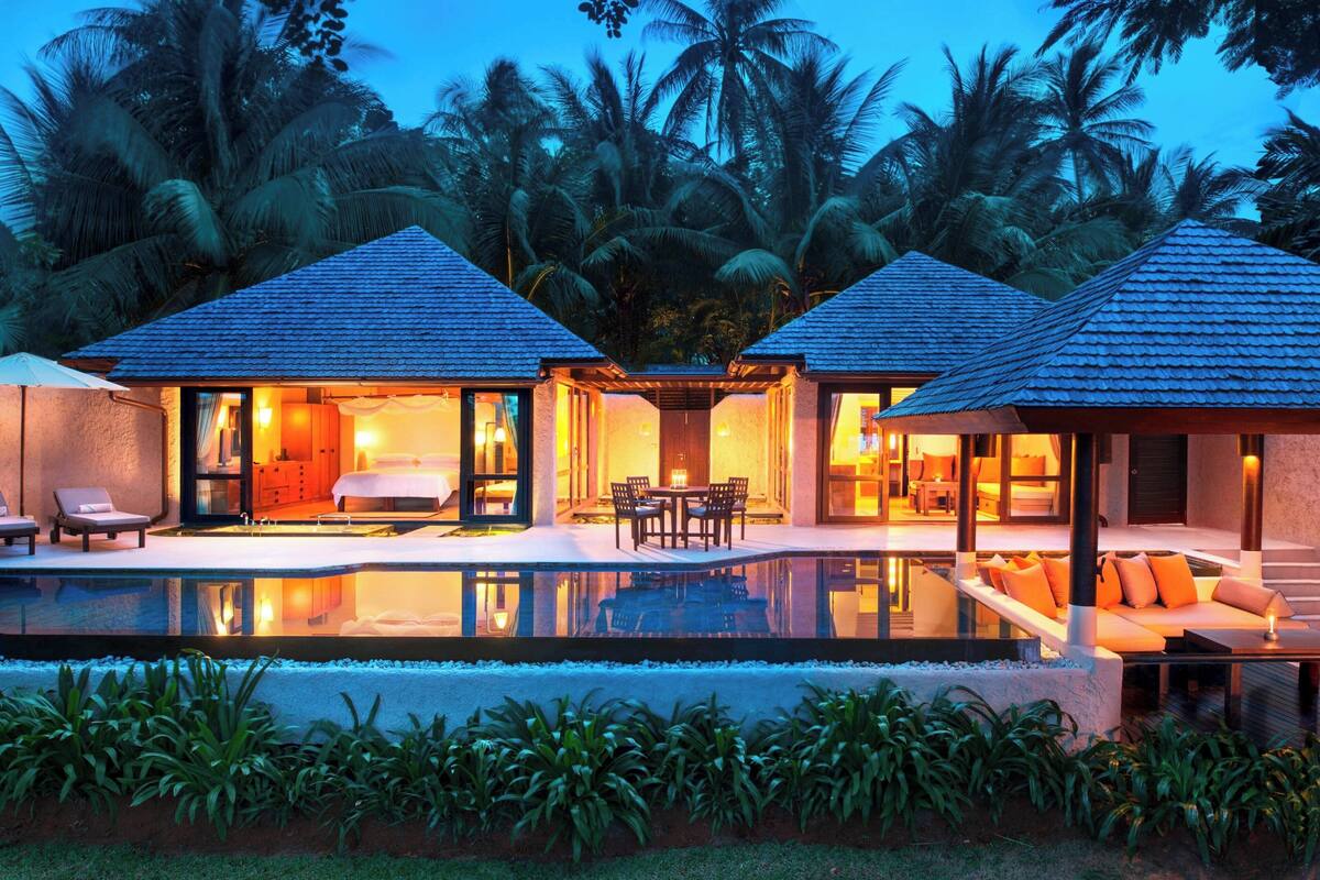 A resort with two guest villas, each with a balcony, a pool, and a view of palm trees.