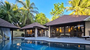Un espace aménagé au bord de la piscine, avec une eau cristalline, des coins salon abrités et des palmiers en arrière-plan.