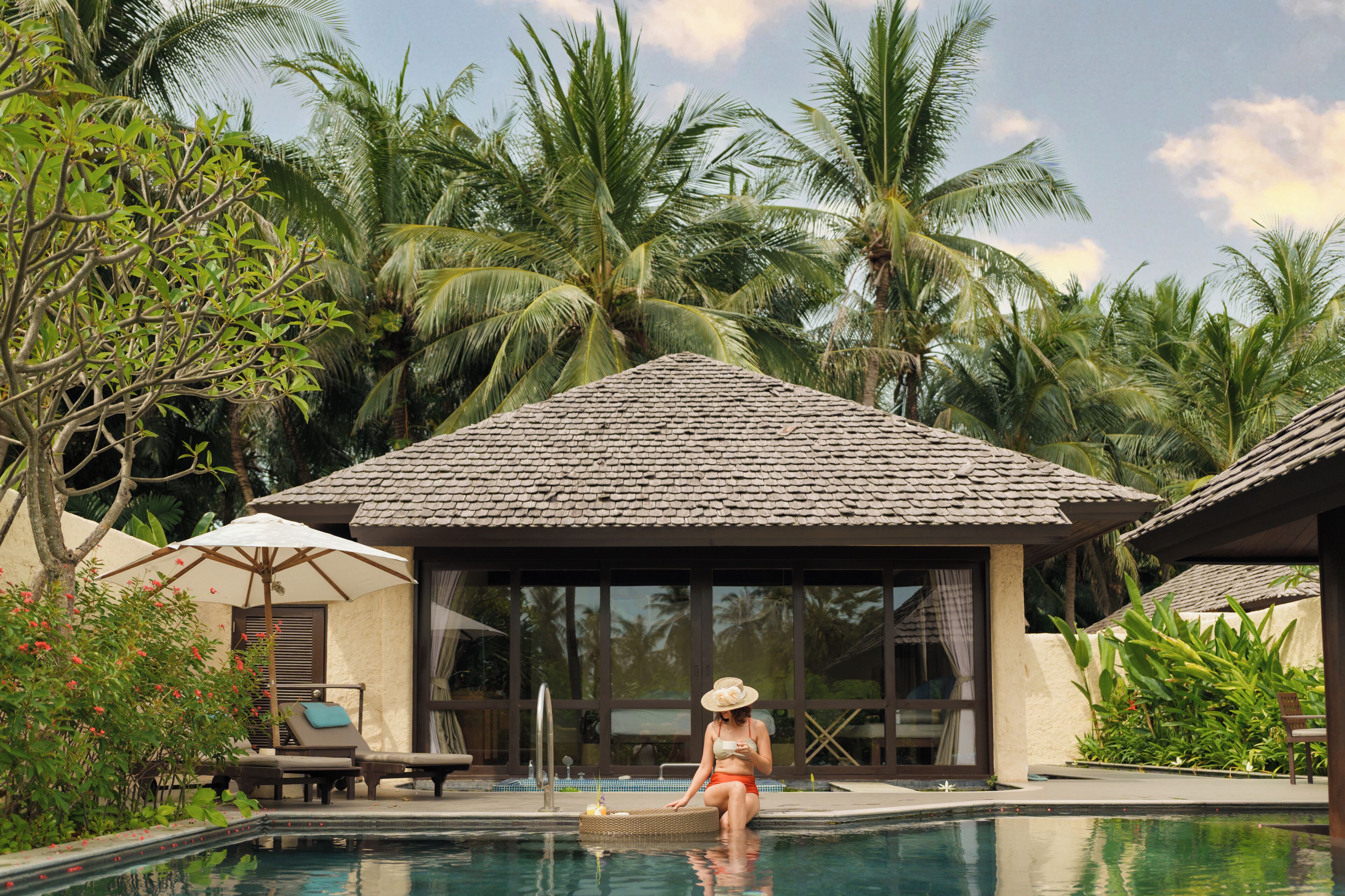 A pool area with a lounge chair, a small hut, and lush tropical vegetation.