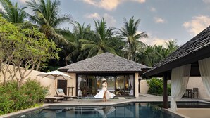 Un espace piscine avec des chaises longues, un coin salon abrité et un bâtiment doté d’un toit en tuiles.