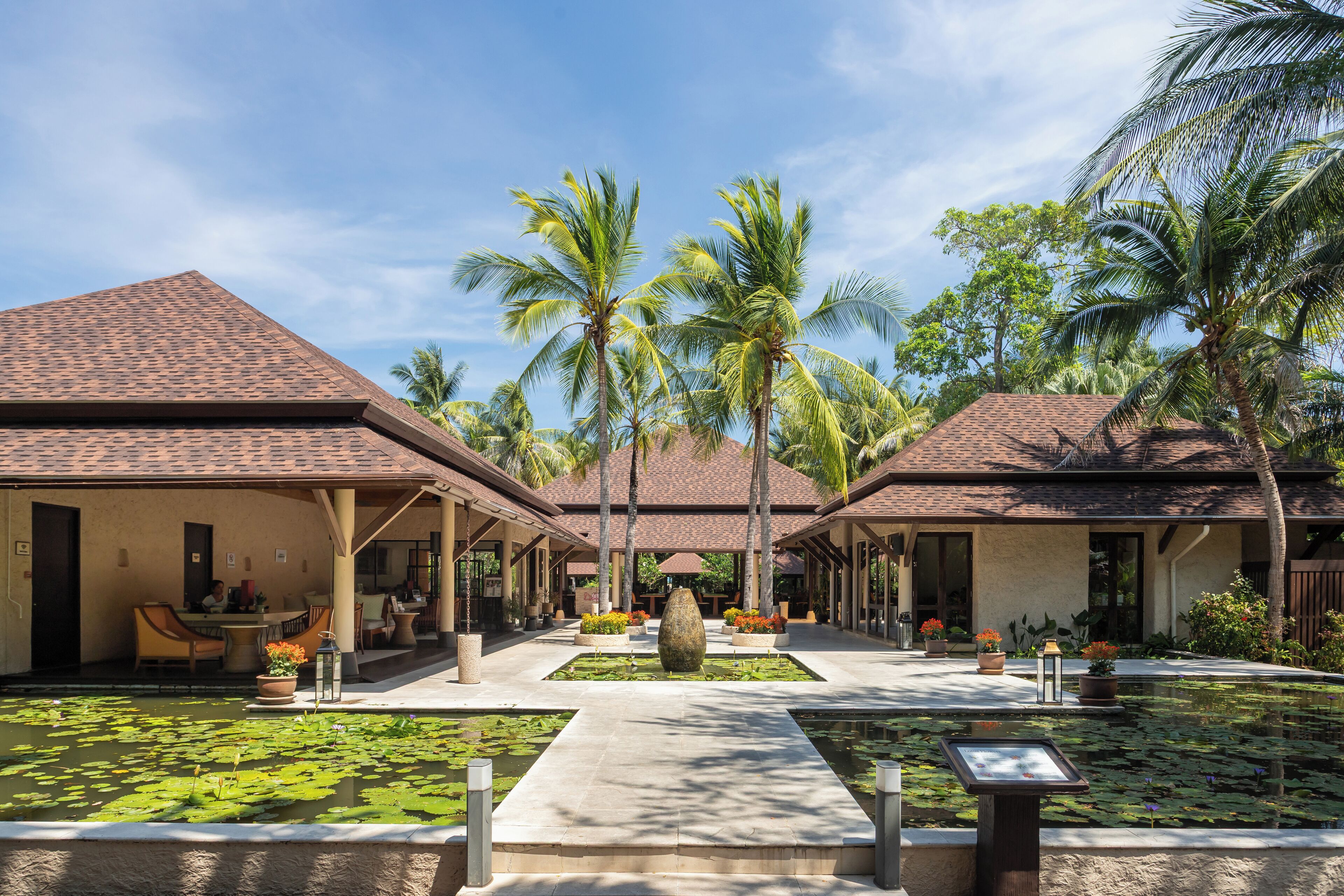 Ein Resort mit zweigeschossigen Gebäuden, einem zentralen Innenhof mit Wasserspiel und Palmen.