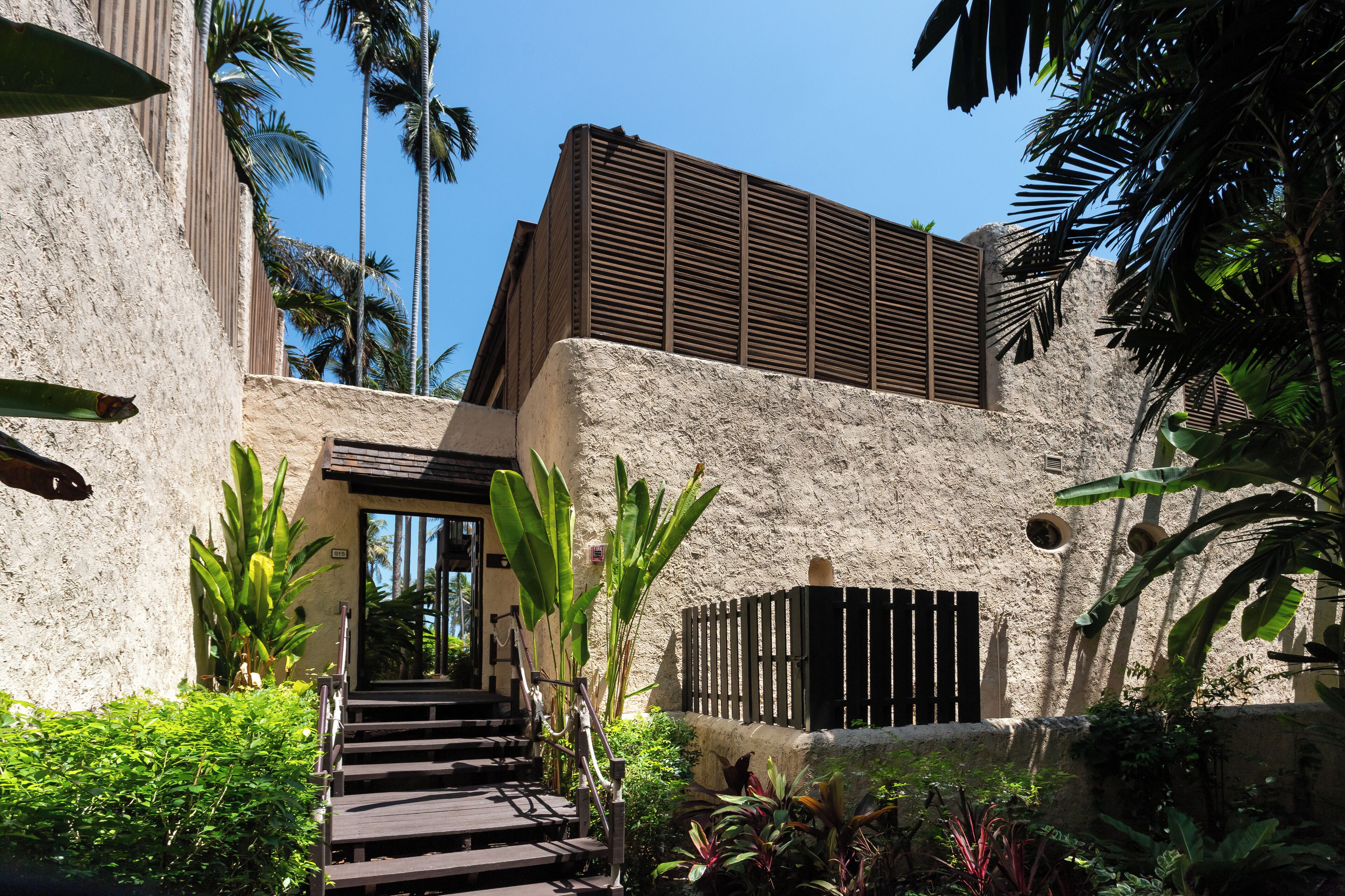 A modern building with a stone facade, a wooden staircase, and tropical plants.