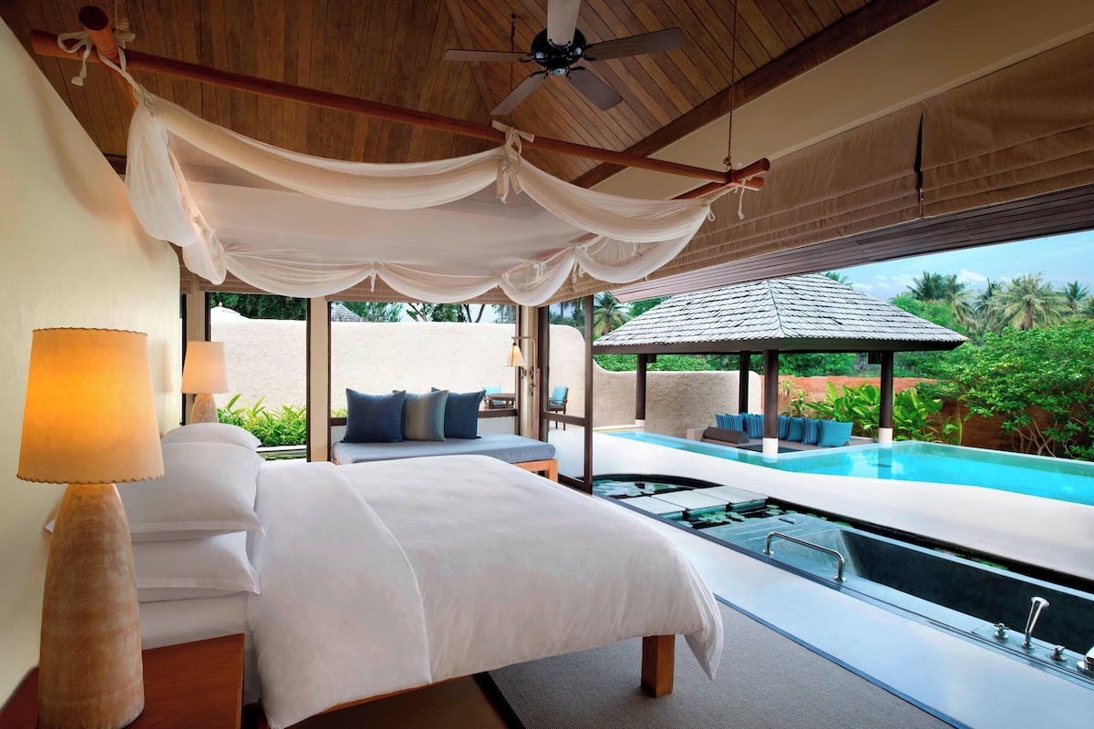 A bedroom with a large bed, a ceiling fan, and a view of an infinity pool.