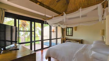 Un dormitorio con cama, televisión, escritorio y ventana con vistas a palmeras.