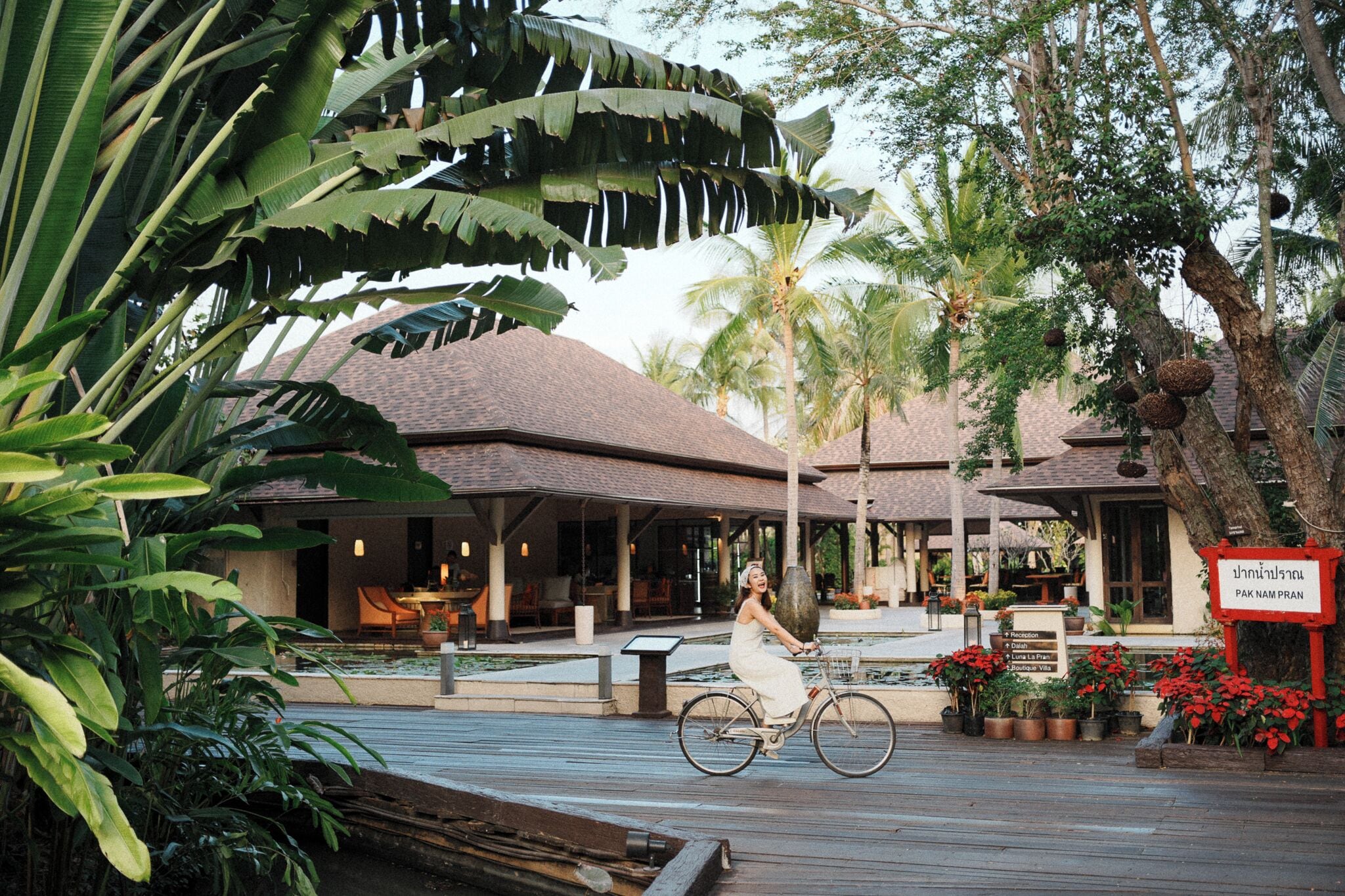A tropical resort with a covered outdoor seating area, a sign indicating 'Pakalut Pran', and lush greenery.