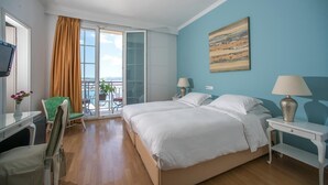 Una habitación de hotel con una cama, dos mesitas de noche con lámparas, un escritorio con una silla, una silla verde, una ventana con cortinas y un cuadro en la pared.