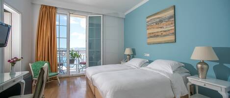 A hotel room with a bed, two bedside tables with lamps, a desk with a chair, a green chair, a window with curtains, and a painting on the wall.