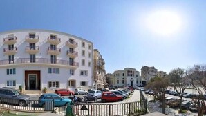 Un hotel con fachada curva, varios balcones y un estacionamiento con algunos coches.