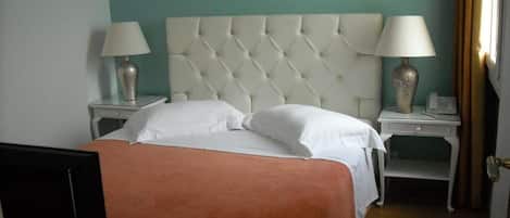 A neatly made bed with white linens, two bedside tables with lamps, and a teal-colored wall.