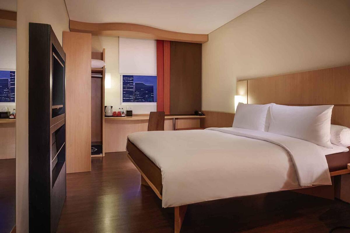 Habitación de hotel con cama, escritorio, silla, ventana y vistas a la ciudad, además de un armario.