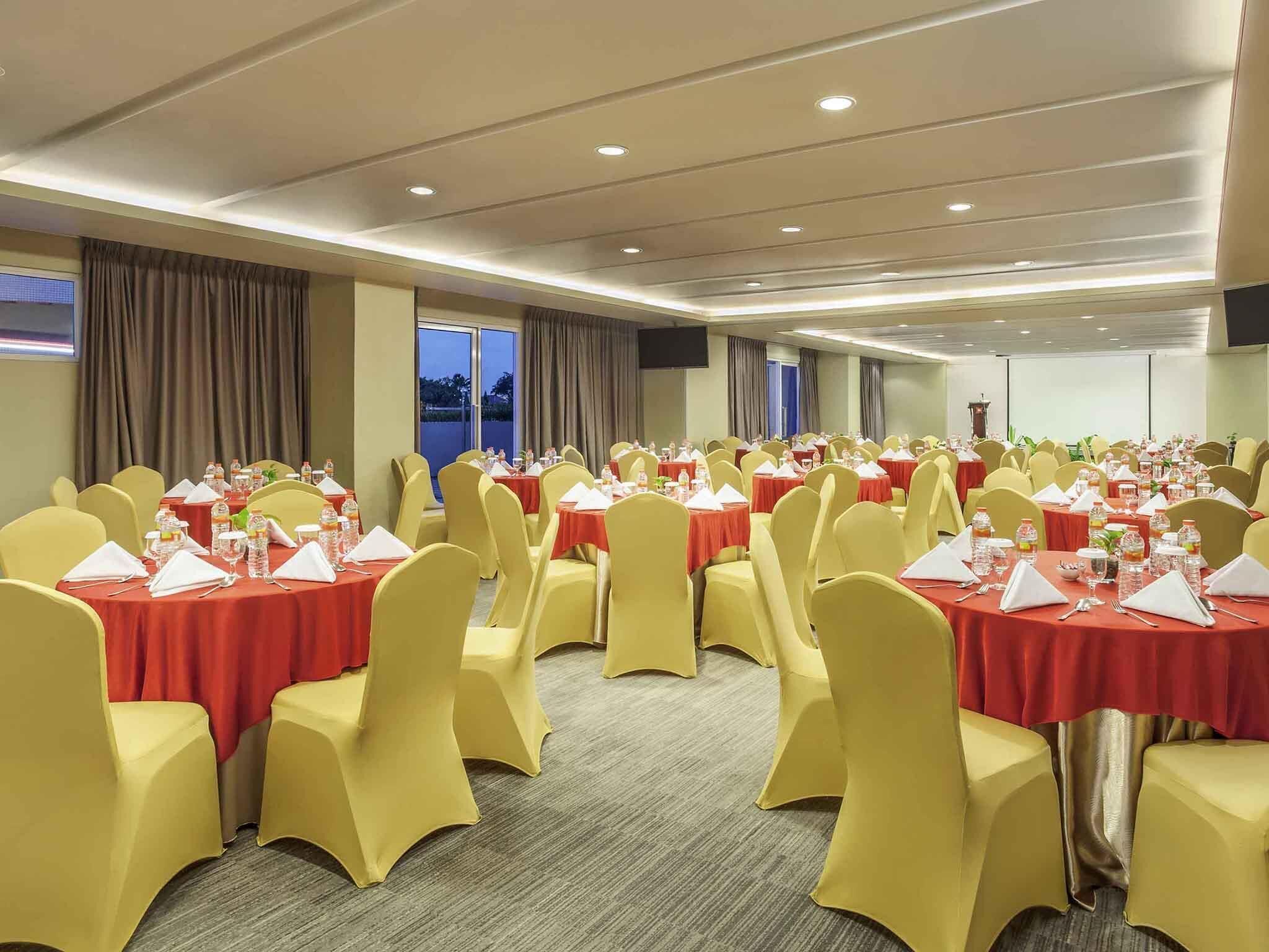 Un salón de conferencias con mesas redondas, sillas amarillas y manteles rojos.