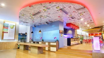 Eine moderne Hotelhalle mit Rezeption, Sitzgelegenheiten und einer Decke mit Zeitungsausschnitten.