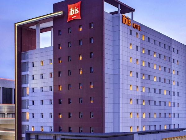 A modern hotel building with a prominent 'ibis Hotels' sign, multiple floors, and a grid-like facade.
