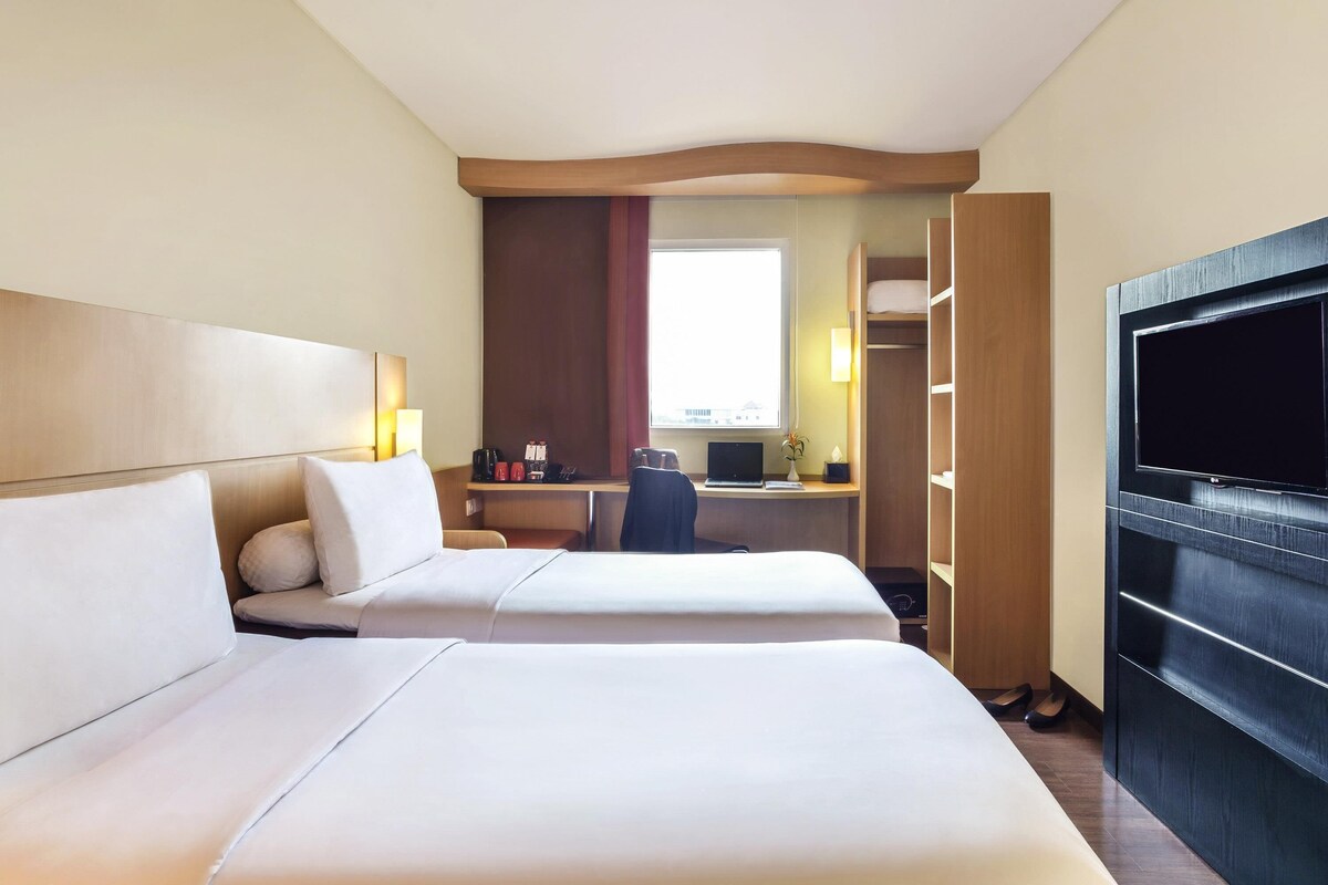 Une chambre d’hôtel avec deux lits, un bureau avec un ordinateur portable, une télévision et une armoire.