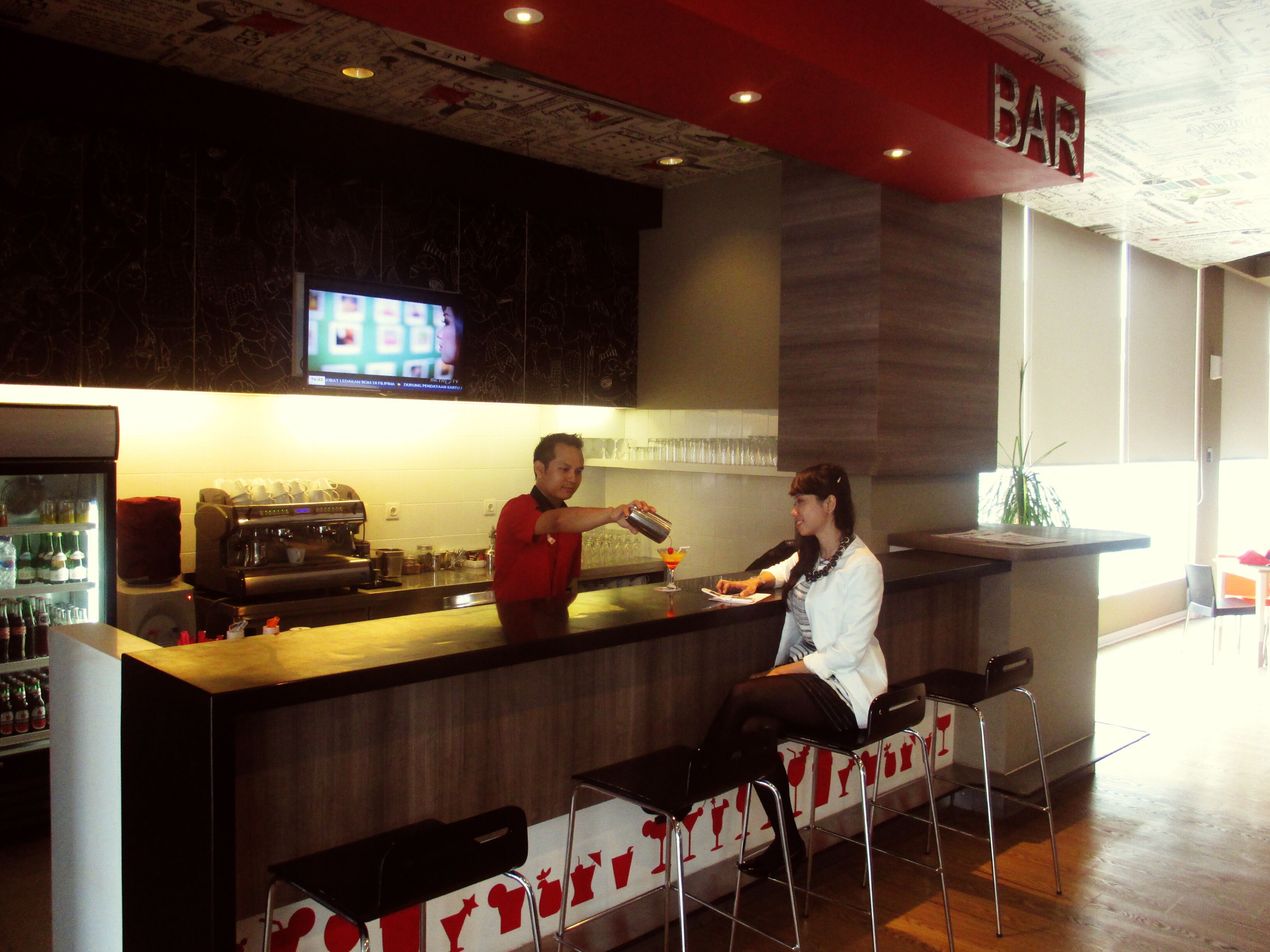 A bar area with a counter, bar stools, a television screen, and a menu board.