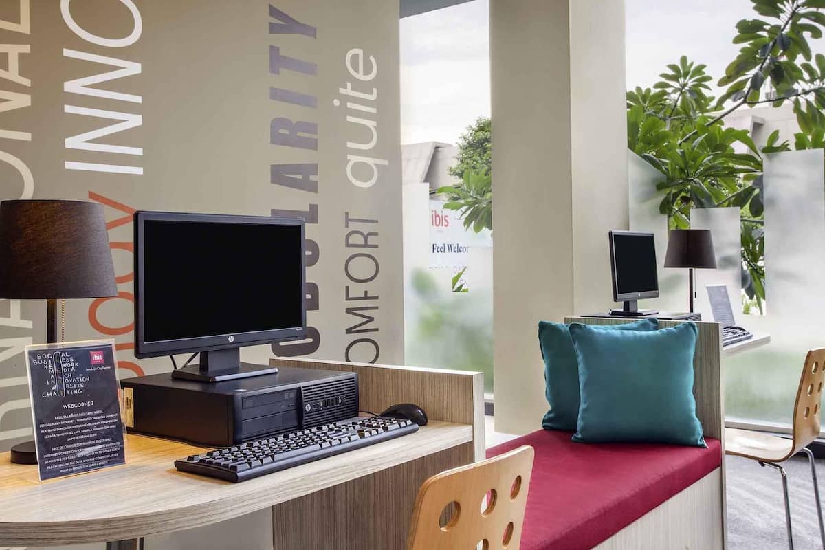 Ein Hotelrezeptionstresen mit Computer, Tastatur, Schreibtischlampe, Stuhl und einem Fenster mit Pflanzen.