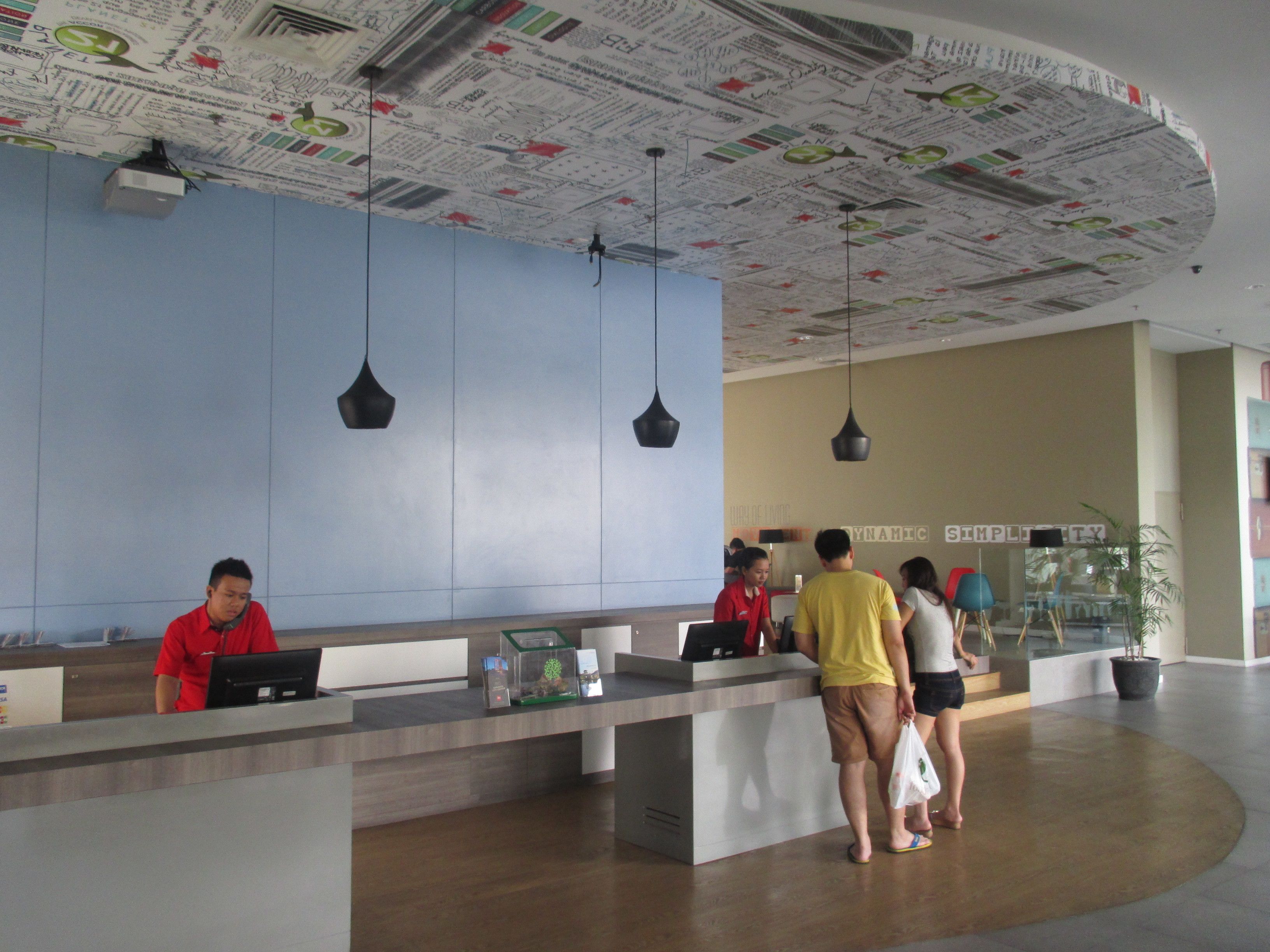 A reception area with a modern design, featuring a blue wall, a ceiling with a newspaper print, and a reception desk.