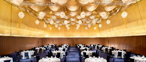A banquet hall with round tables, chairs, and a decorative ceiling.