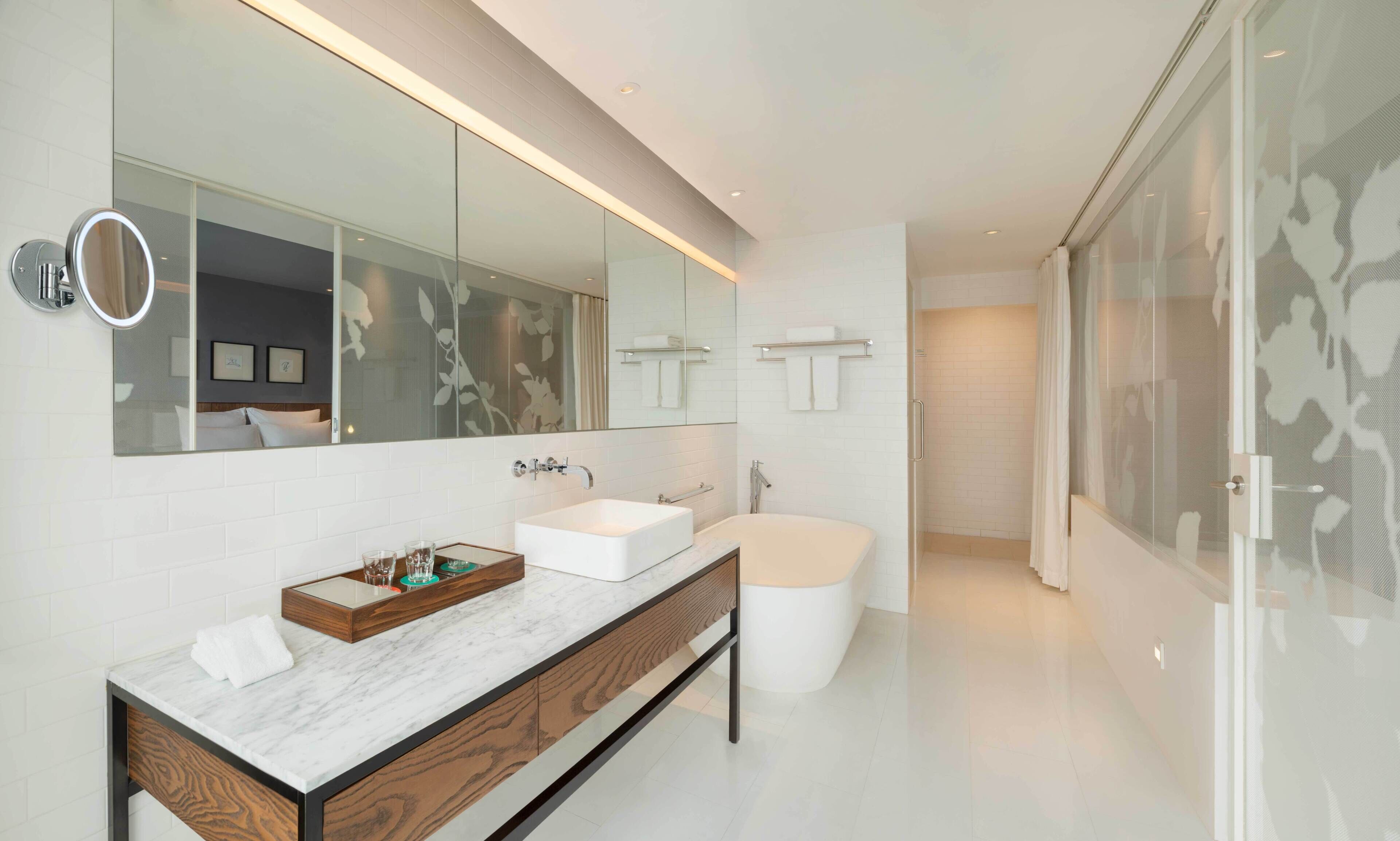 A modern bathroom with a large mirror, two sinks, a bathtub, and a shower.