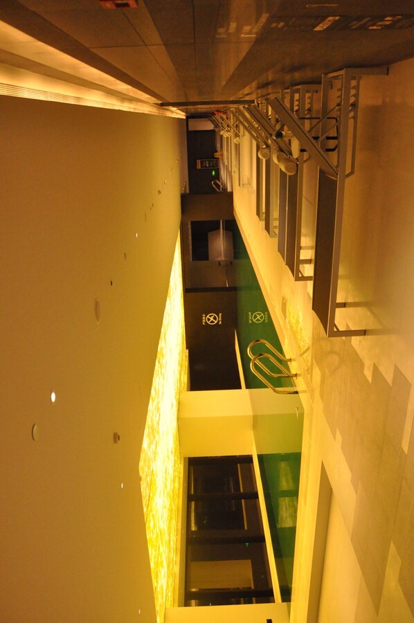 Un pasillo con una escalera, un letrero de seguridad verde y una barandilla metálica.